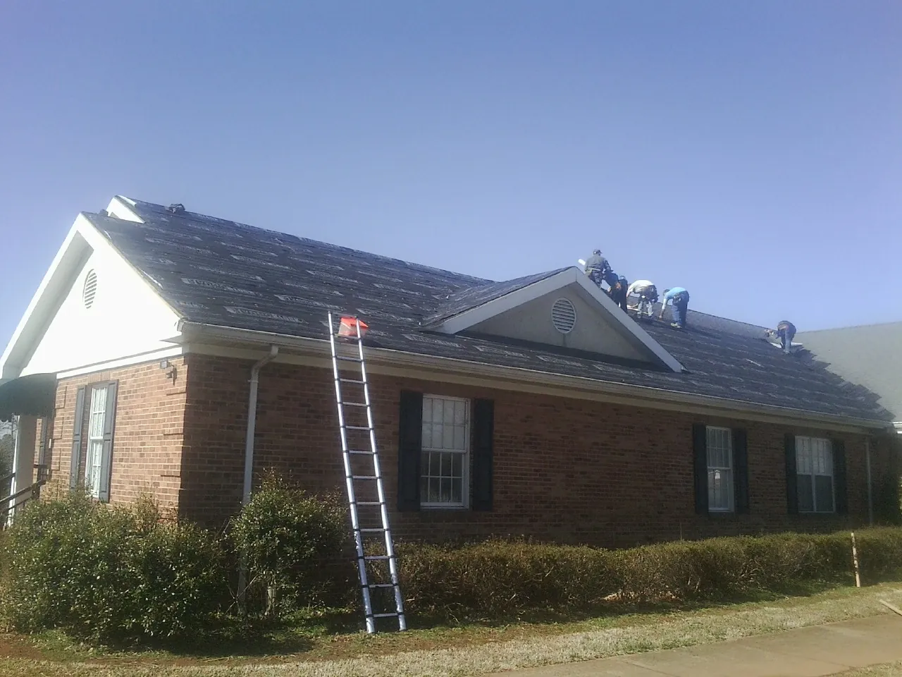 Crew tearing shingles off a brick ranch roof with a ladder set — Emergency Roof Repair work by our crew in Mount Victory