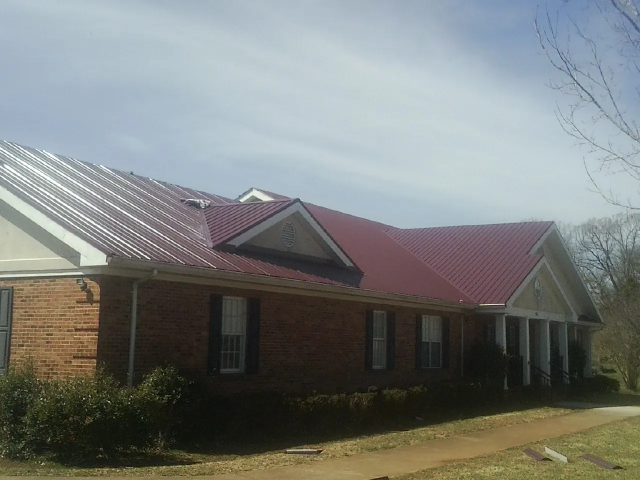 Red metal roof with gabled entries on a long brick building, from a Hail Damage Roof Repair job in Mount Victory