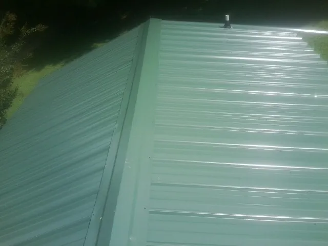 New green metal panels meeting at the ridge of a roof — Flat Roof Repair work by our crew in Mount Victory