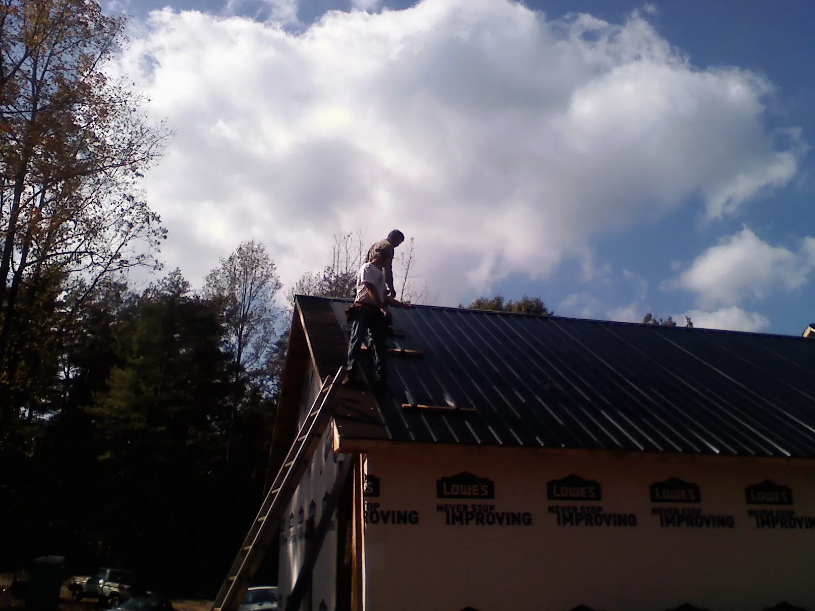 Roofer fastening dark metal panels high against a cloudy sky, from a Roof Inspection job in Mount Victory