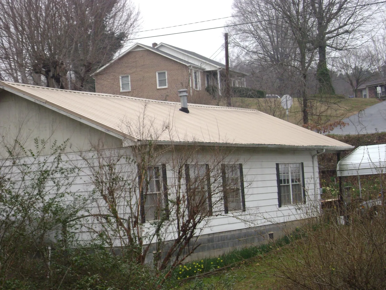 Tan metal roof on a white sided house set into a hillside — Commercial Roofing by Roofing Brothers in Mount Victory
