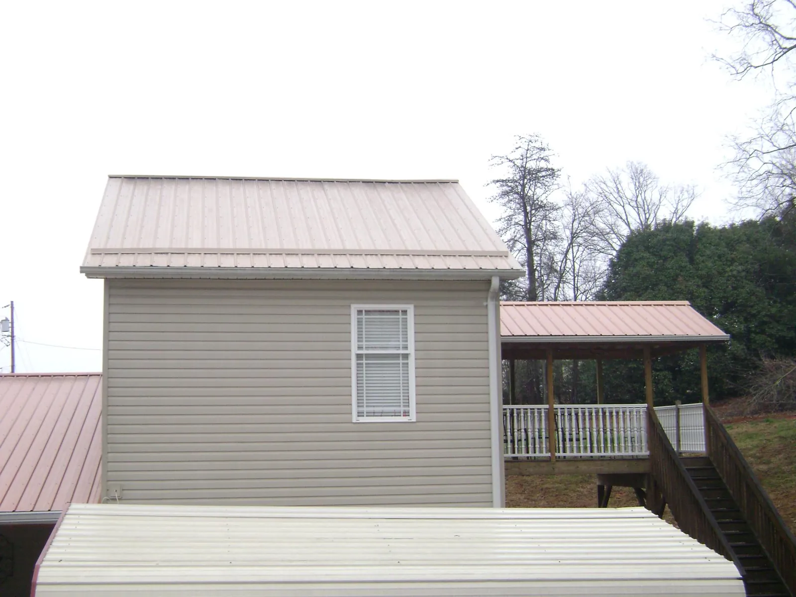 Tan metal roofs on a two story addition and attached porch, from a Roof Replacement job in Mount Victory